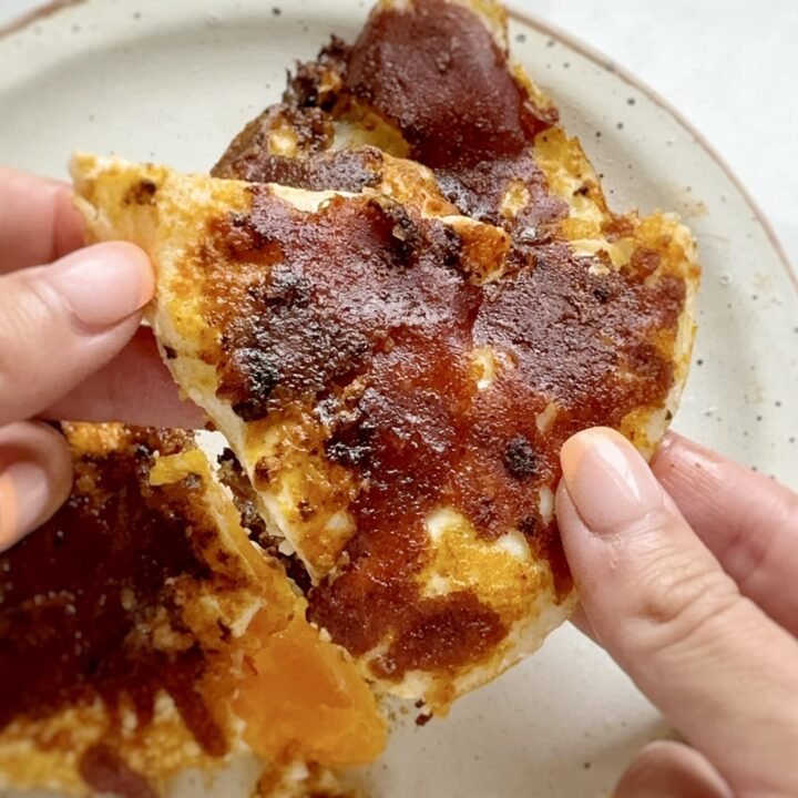 Close-up of crispy mozzarella and red pesto eggs in a frying pan, with golden cheese edges, vibrant red pesto base, and perfectly cooked sunny-side-up eggs. Preguntar a ChatGPT