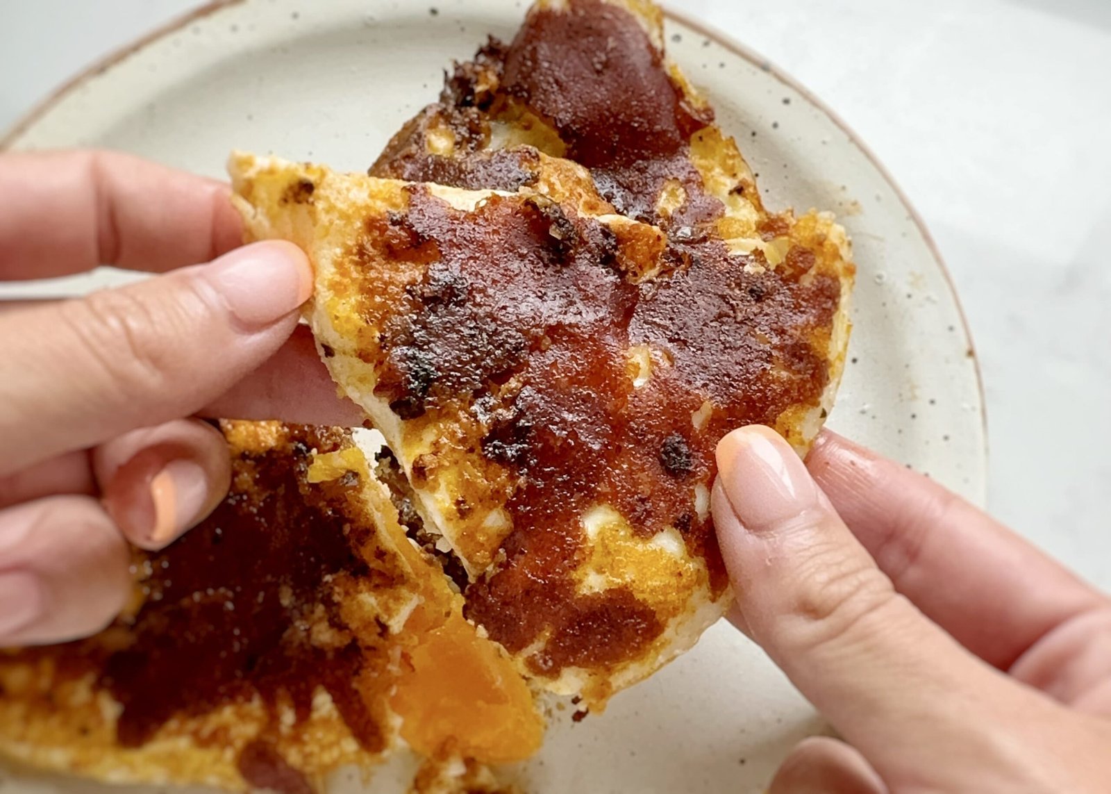 Close-up of crispy mozzarella and red pesto eggs in a frying pan, with golden cheese edges, vibrant red pesto base, and perfectly cooked sunny-side-up eggs. Preguntar a ChatGPT