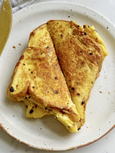 Golden, crispy egg sandwich filled with fluffy scrambled eggs, melted cheese, and savoury ham, served hot on a white plate.