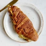 golden Cheese Egg Croissant filled with fluffy eggs and melted cheddar, served warm and flaky on a plate.
