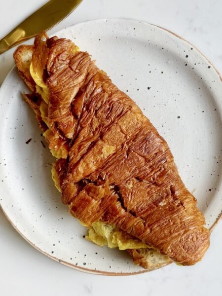golden Cheese Egg Croissant filled with fluffy eggs and melted cheddar, served warm and flaky on a plate.