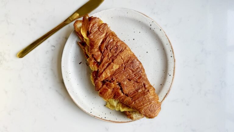 golden Cheese Egg Croissant filled with fluffy eggs and melted cheddar, served warm and flaky on a plate.