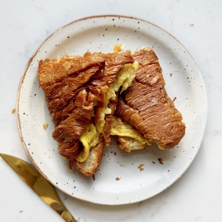 golden Cheese Egg Croissant filled with fluffy eggs and melted cheddar, served warm and flaky on a plate.