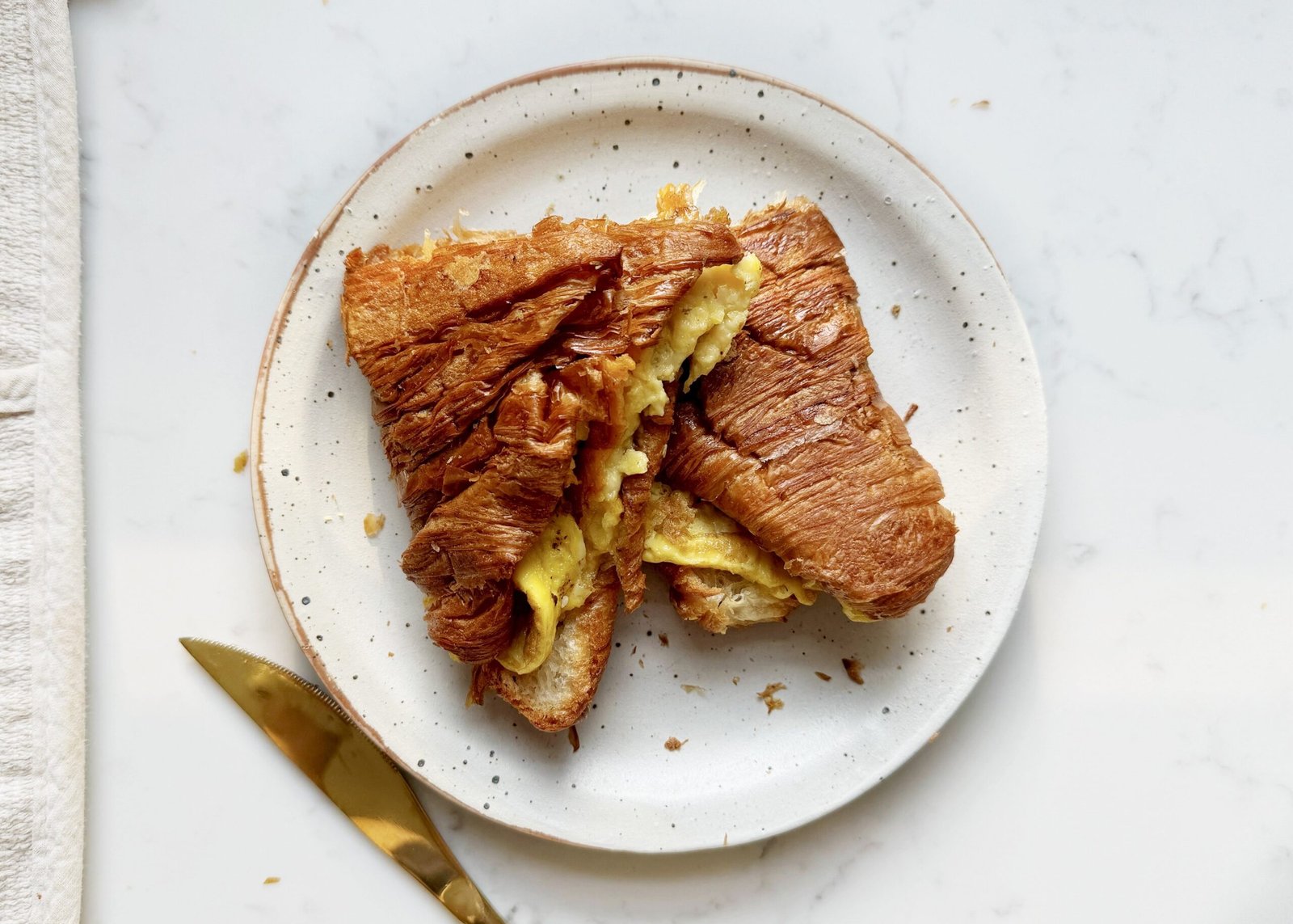 golden Cheese Egg Croissant filled with fluffy eggs and melted cheddar, served warm and flaky on a plate.