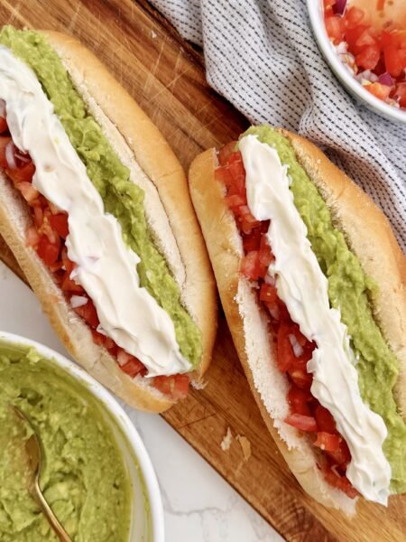 A Chilean Completo Italiano hot dog in a soft bun, topped with mashed avocado, fresh diced tomato, and zigzagged mayonnaise.
