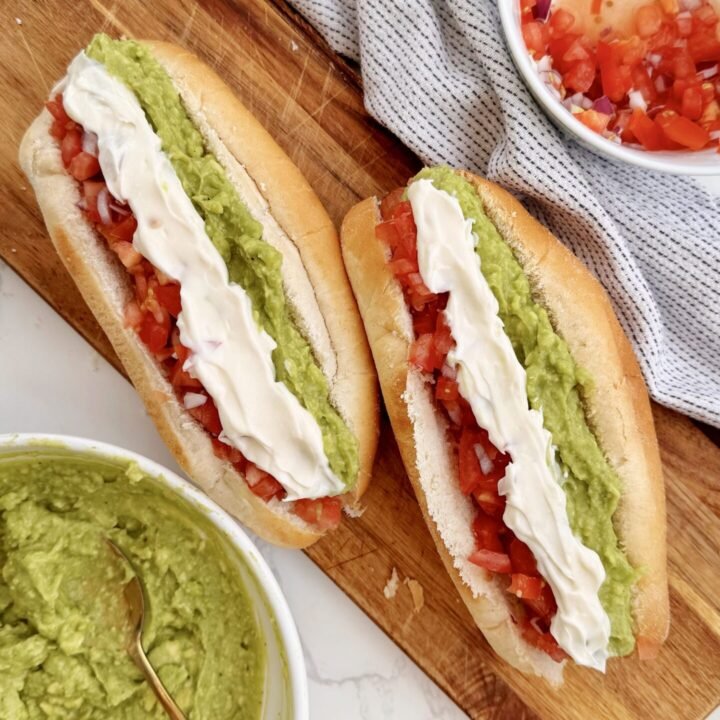 A Chilean Completo Italiano hot dog in a soft bun, topped with mashed avocado, fresh diced tomato, and zigzagged mayonnaise.