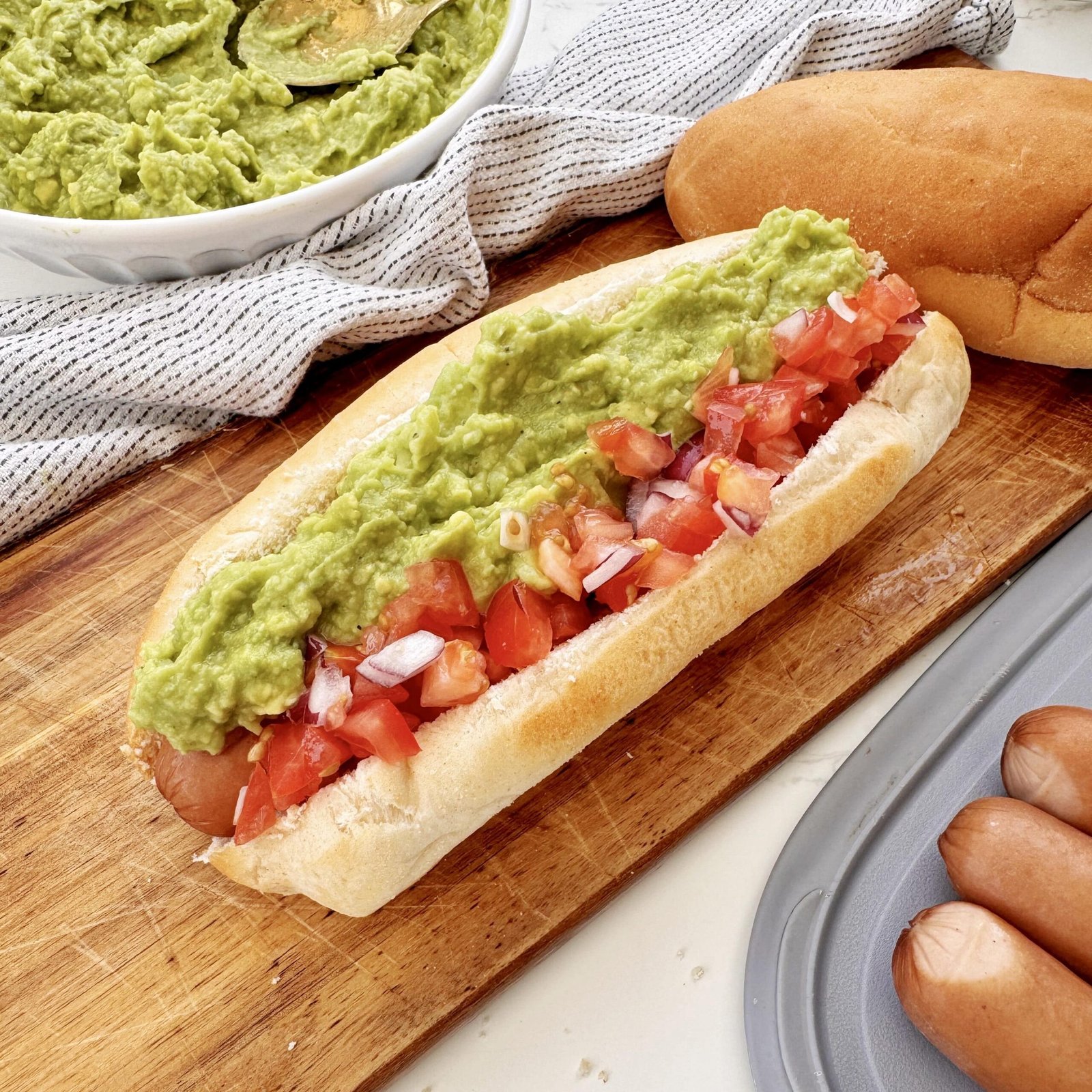 A Chilean Completo Italiano hot dog in a soft bun, topped with mashed avocado, fresh diced tomato, and zigzagged mayonnaise.