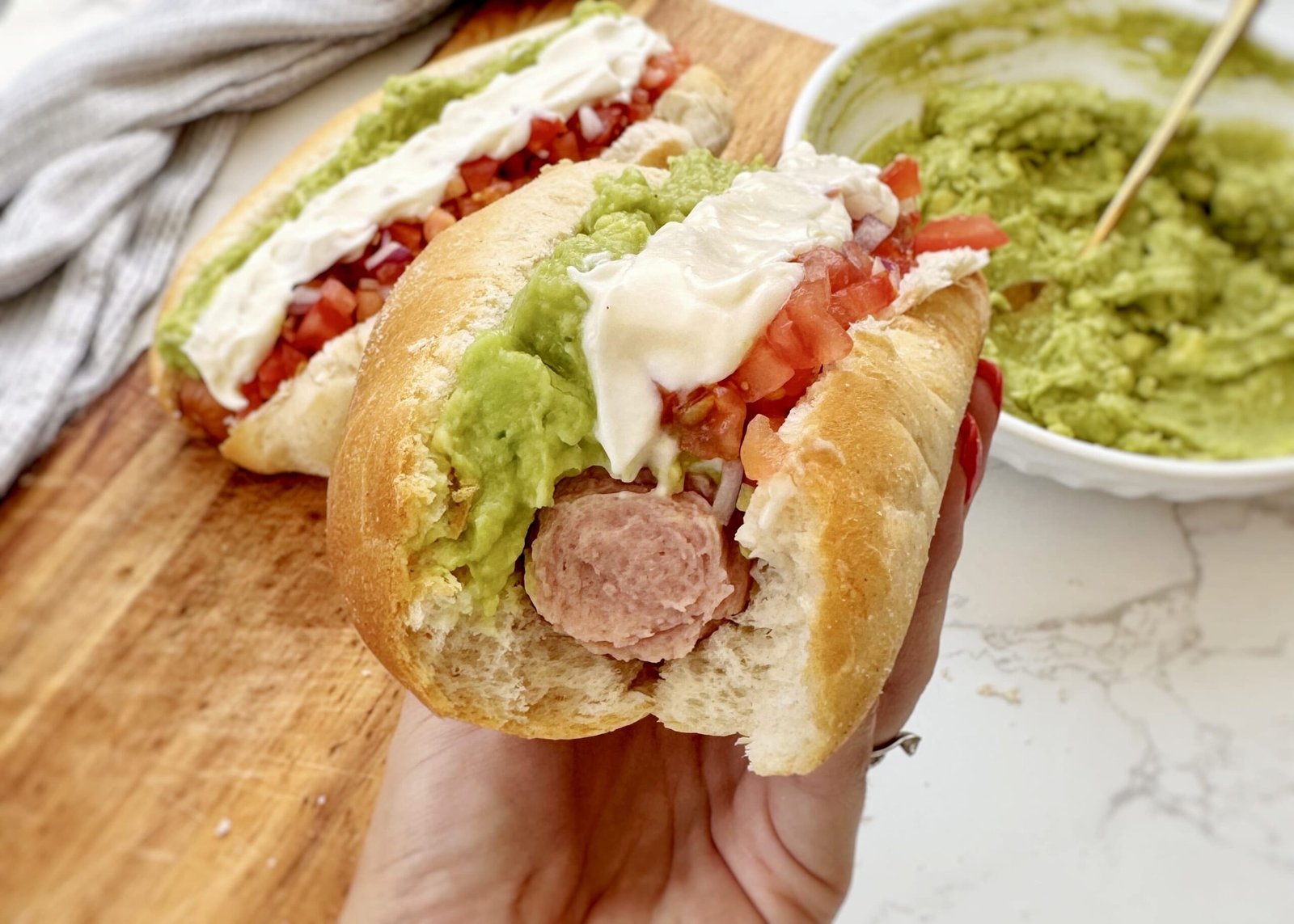 A Chilean Completo Italiano hot dog in a soft bun, topped with mashed avocado, fresh diced tomato, and zigzagged mayonnaise.