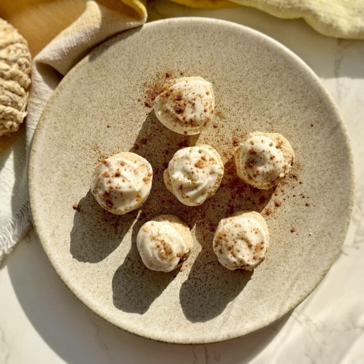 Pumpkin spice cheesecake protein bites coated in cream cheese icing on parchment paper