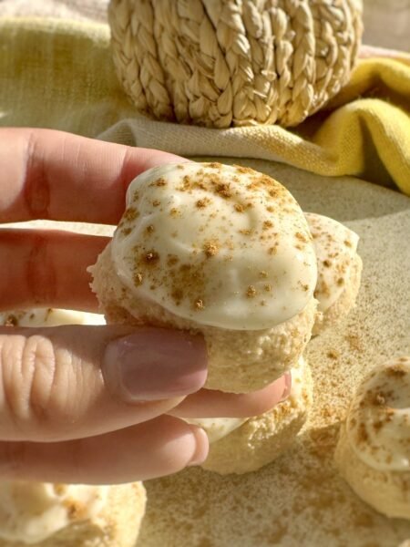 Pumpkin spice cheesecake protein bites coated in cream cheese icing on parchment paper