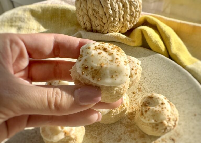 Pumpkin spice cheesecake protein bites coated in cream cheese icing on parchment paper
