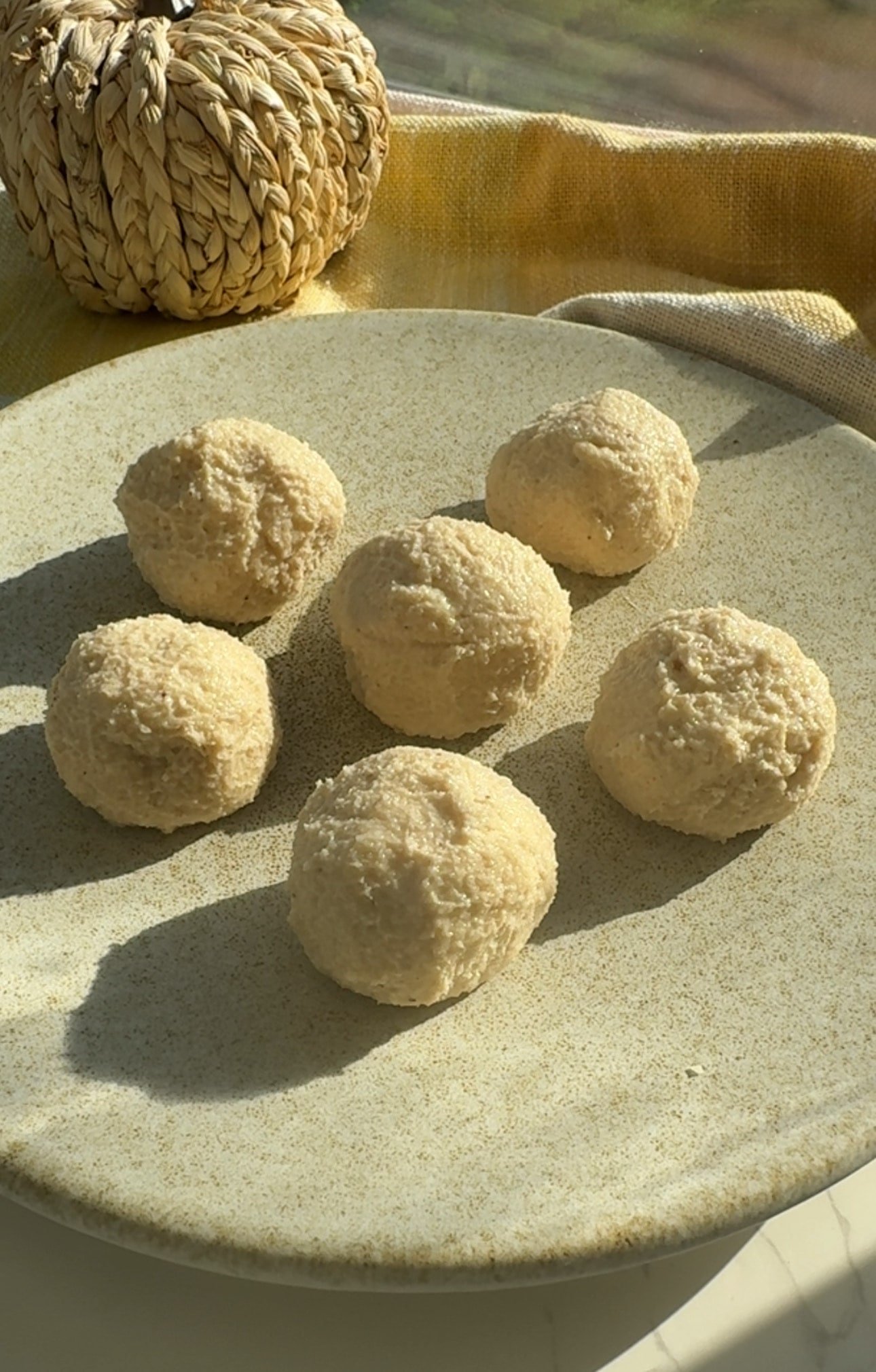 Pumpkin spice cheesecake protein balls coated in cream cheese icing on parchment paper