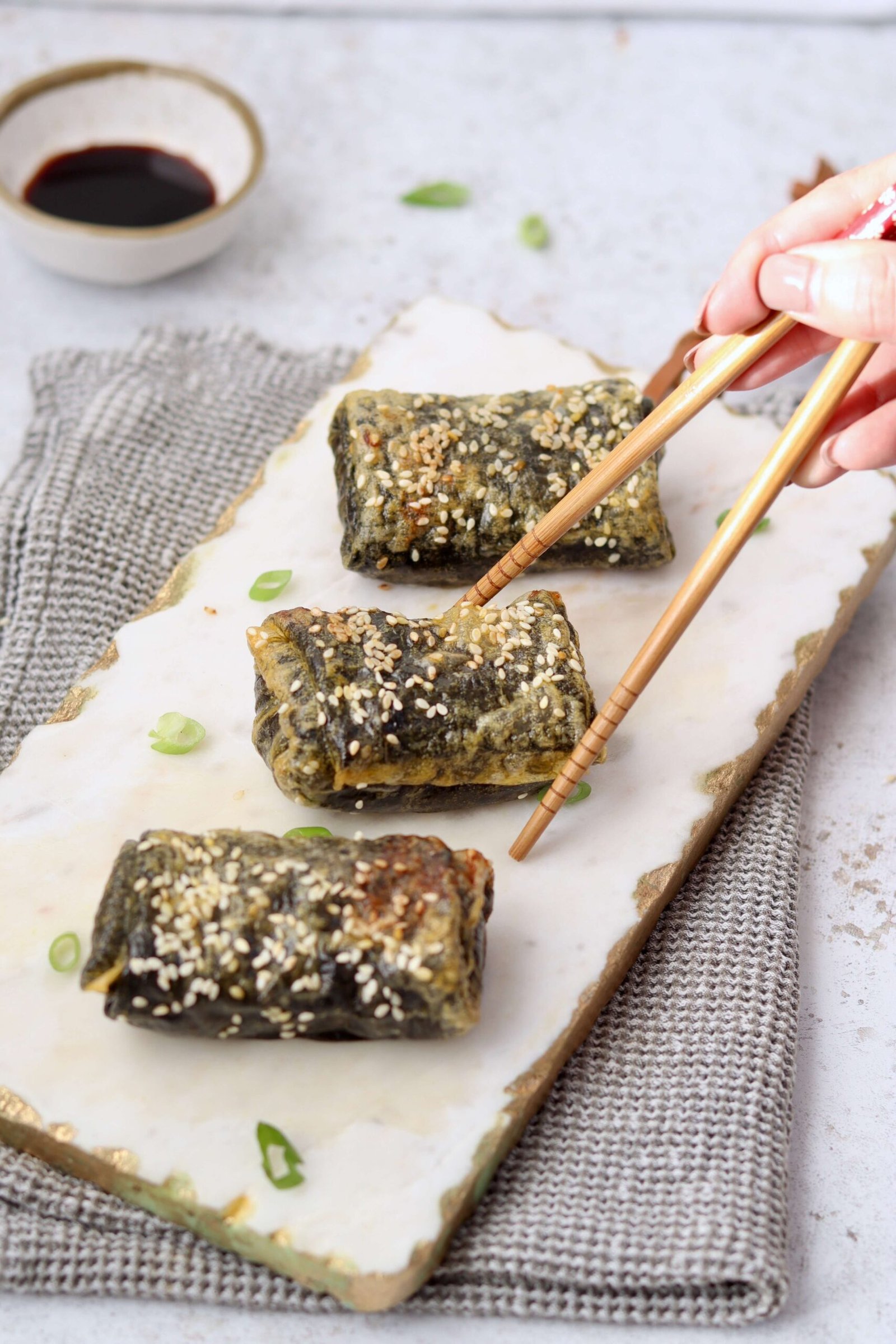 Crispy Spicy Tuna Rice Paper Rolls served on a board with a hand holding chopsticks