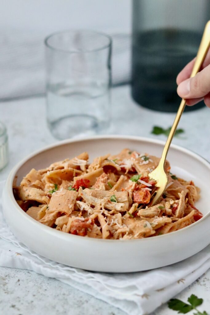 Spicy and creamy chicken Brousin pasta serves on a pasta bowl, a person's hand holding a fork