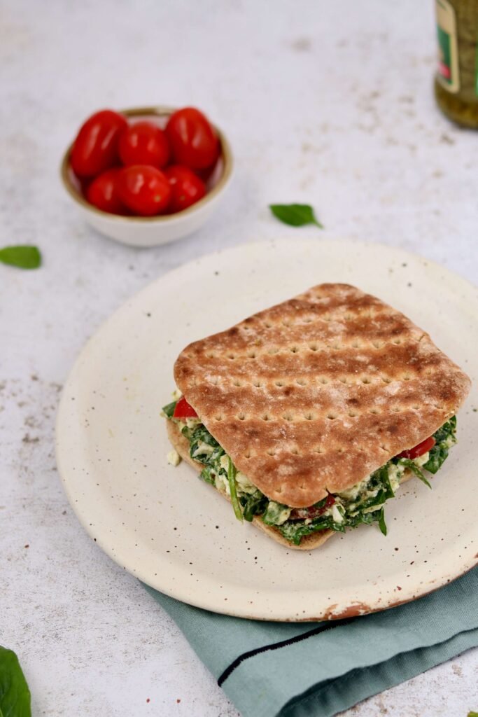 Pesto Chicken Cottage cheese Sandwich served on a plate with a bowl of cheery tomatoes in background