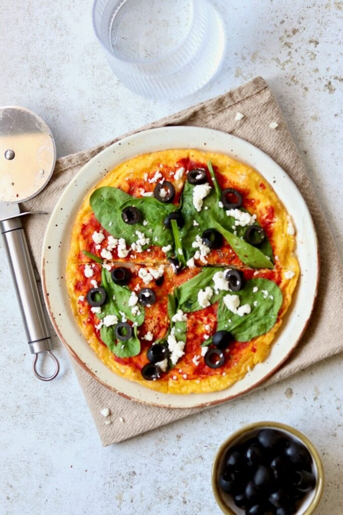 Delicious homemade pizza topped with spinach, olives, and feta cheese, served on a rustic plate with a pizza cutter.