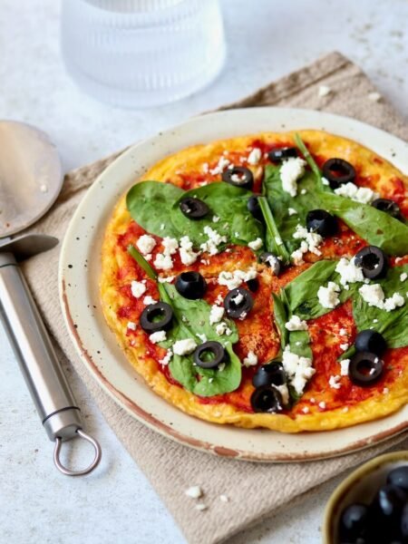 Delicious homemade pizza topped with spinach, black olives, and feta cheese on a rustic plate, served with a pizza cutter.