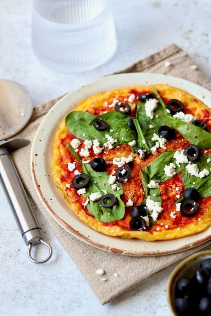 Delicious homemade pizza topped with spinach, black olives, and feta cheese on a rustic plate, served with a pizza cutter.