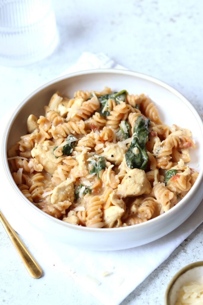 Creamy Tuscan chicken pasta in a white bowl, showing tender chicken pieces, spinach and light cottage cheese sauce