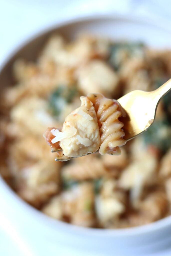 Forkful of high protein Tuscan chicken pasta with tender chicken and creamy sauce, held over the bowl