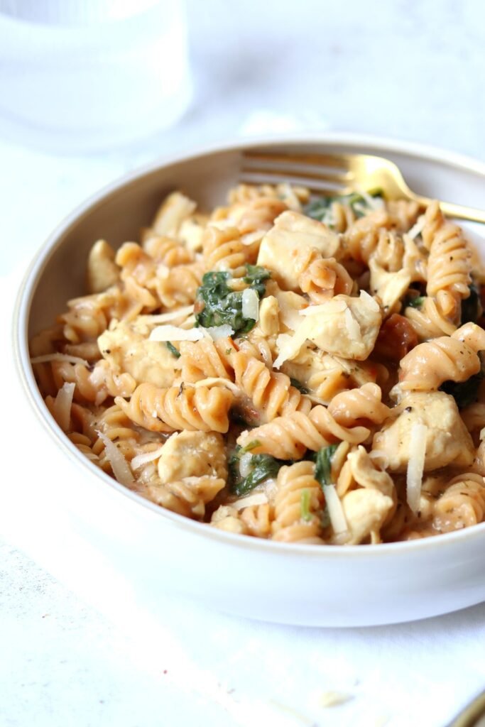 Close-up of Tuscan chicken pasta coated in creamy cottage cheese sauce, served in a white bowl with a gold fork