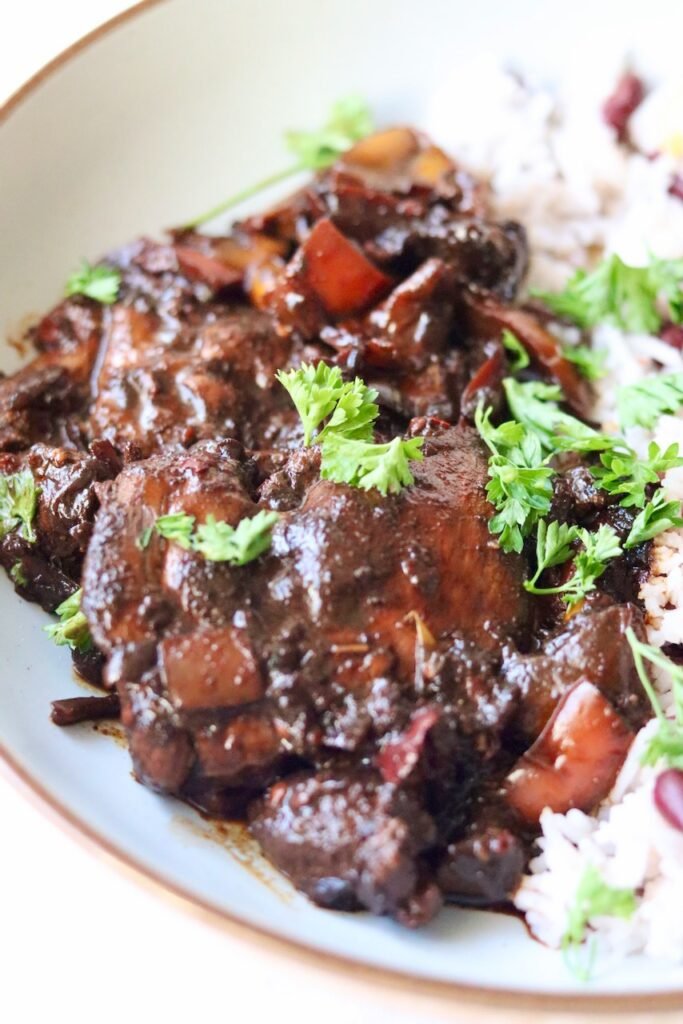 Caribbean brown stew chicken served over rice and peas with fresh parsley