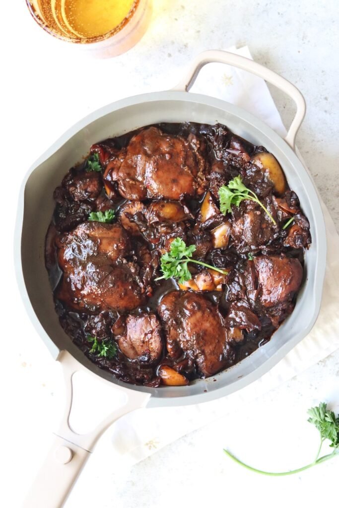 Brown stew chicken simmering in a shallow pan with peppers and onions