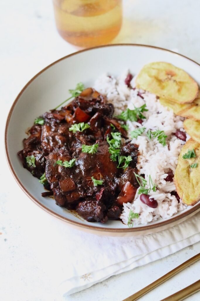 Bowl of brown stew chicken with rice and peas and fried plantain