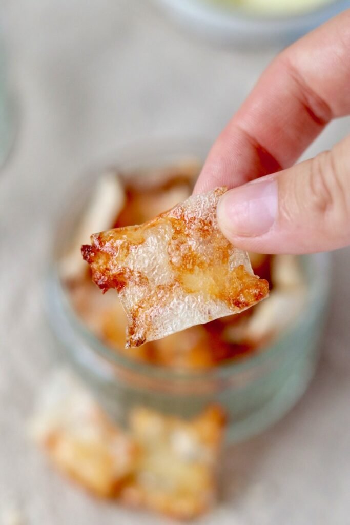 Crispy cheese and onion rice paper chip held up close, showing the melted cheese inside