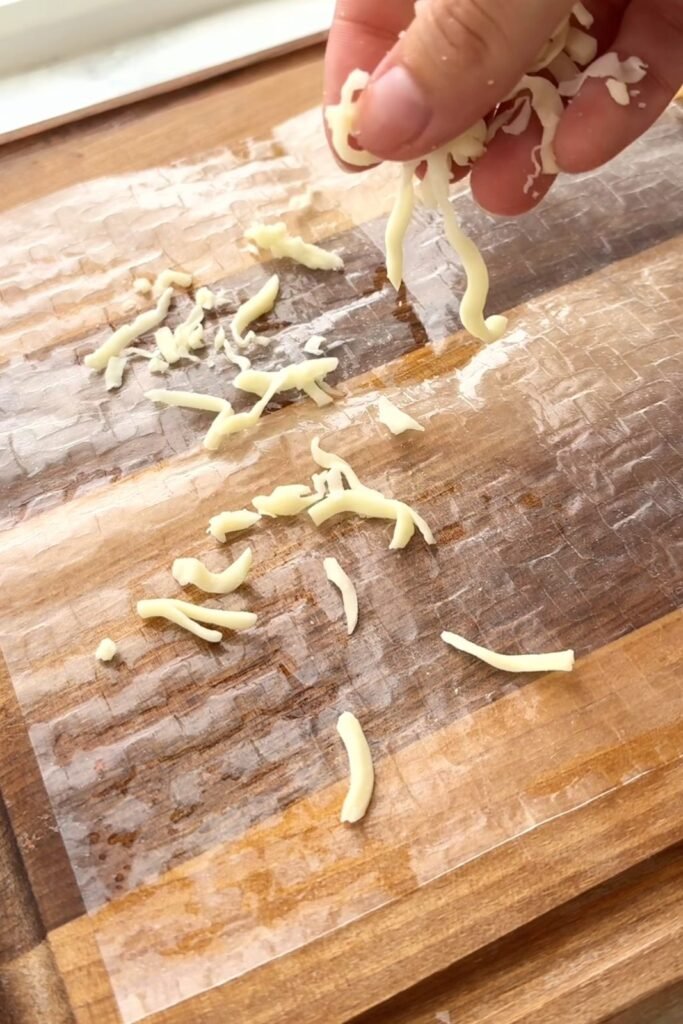 Close-up of grated cheese and onion granules scattered over rice paper before cooking