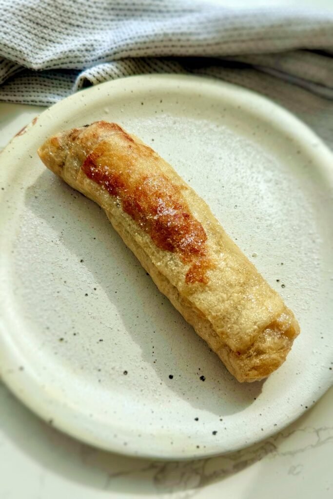 Crispy rice paper banana spring roll on a speckled plate dusted with sweetener