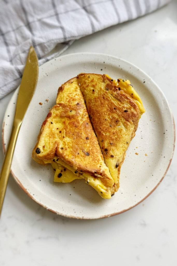 A folded egg sandwich with ham and cheese on a white speckled plate, golden and crispy on the outside.