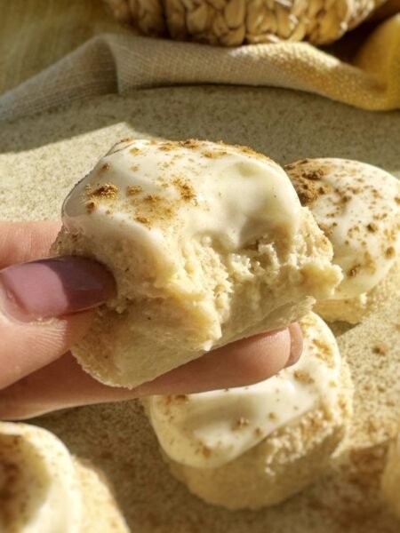 Pumpkin spice cheesecake bites held in one hand, coated in cream cheese icing
