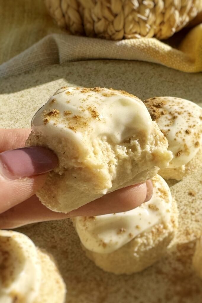 Pumpkin spice cheesecake bites held in one hand, coated in cream cheese icing
