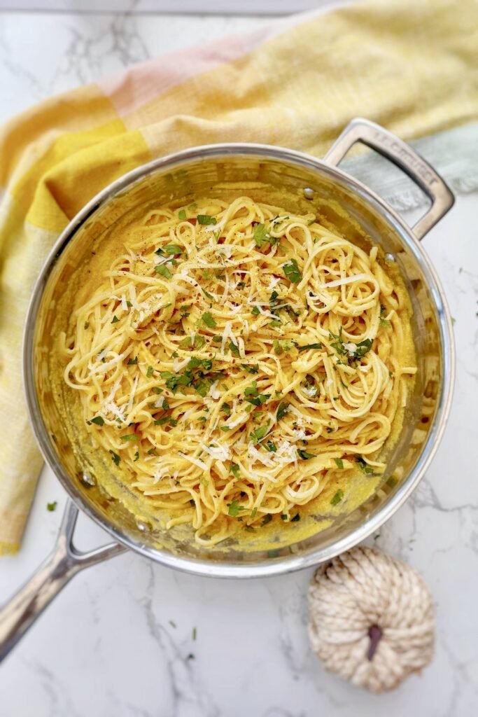 Creamy roasted pumpkin pasta in the pan, topped with parmesan and herbs