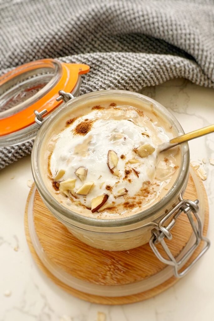 Side angle of a jar of high protein pumpkin spice latte overnight oats with a gold spoon and linen napkin in the background.