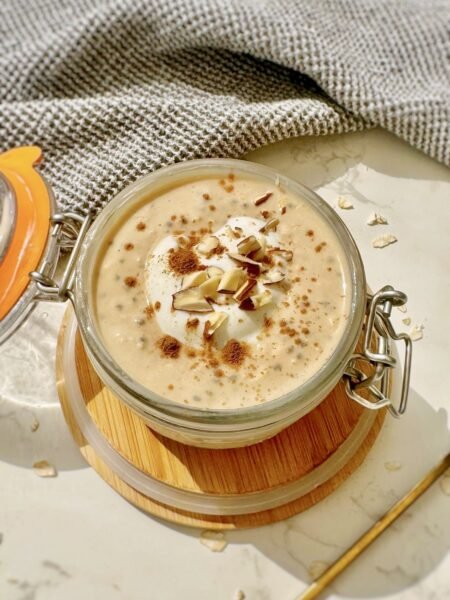 A jar of pumpkin spice latte overnight oats topped with skyr, cinnamon and chopped nuts, with a gold spoon resting inside.