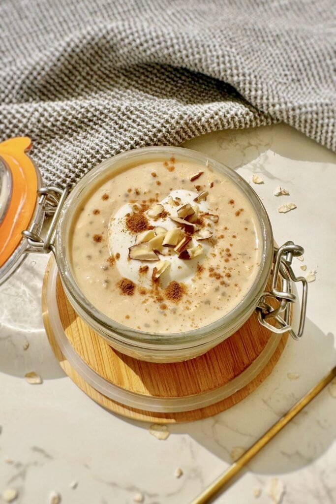 A jar of pumpkin spice latte overnight oats topped with skyr, cinnamon and chopped nuts, with a gold spoon resting inside.
