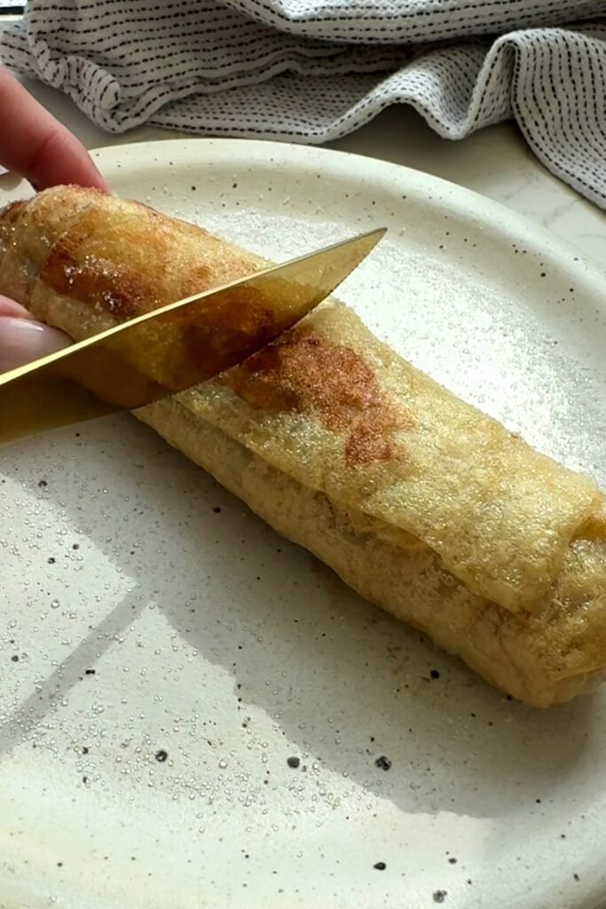Slicing into a crispy air fried banana spring roll with a gold knife