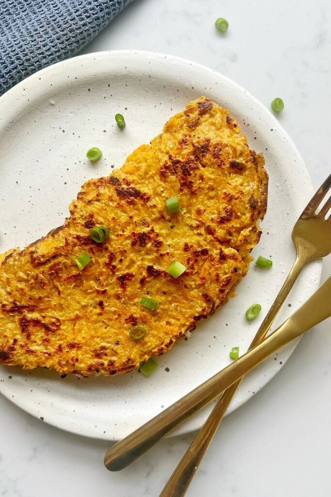 Sweet potato wrap folded over on a speckled plate with spring onion and a gold fork