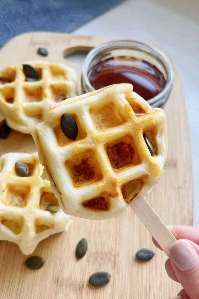 Hand holding an apple waffle pop above a board of waffle pops