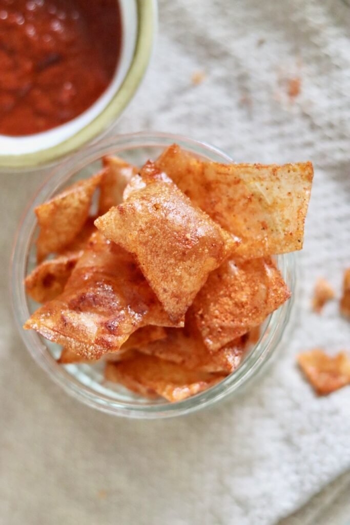 BBQ rice paper chips in a glass bowl with a dish of BBQ sauce behind
