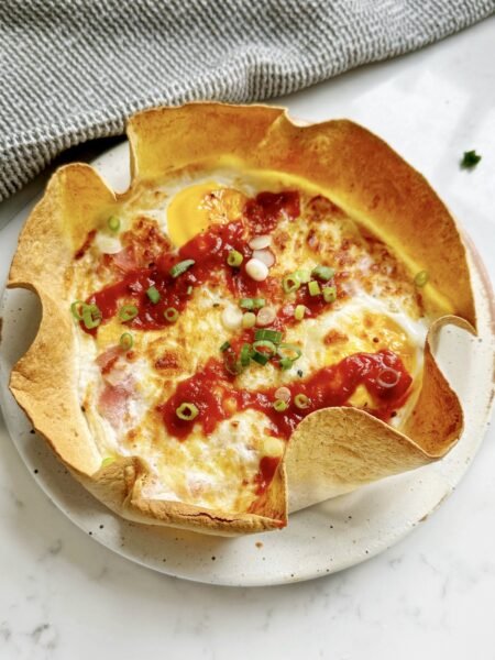 Ham and cheese tortilla quiche in a tortilla case on a speckled plate, topped with ketchup and spring onion