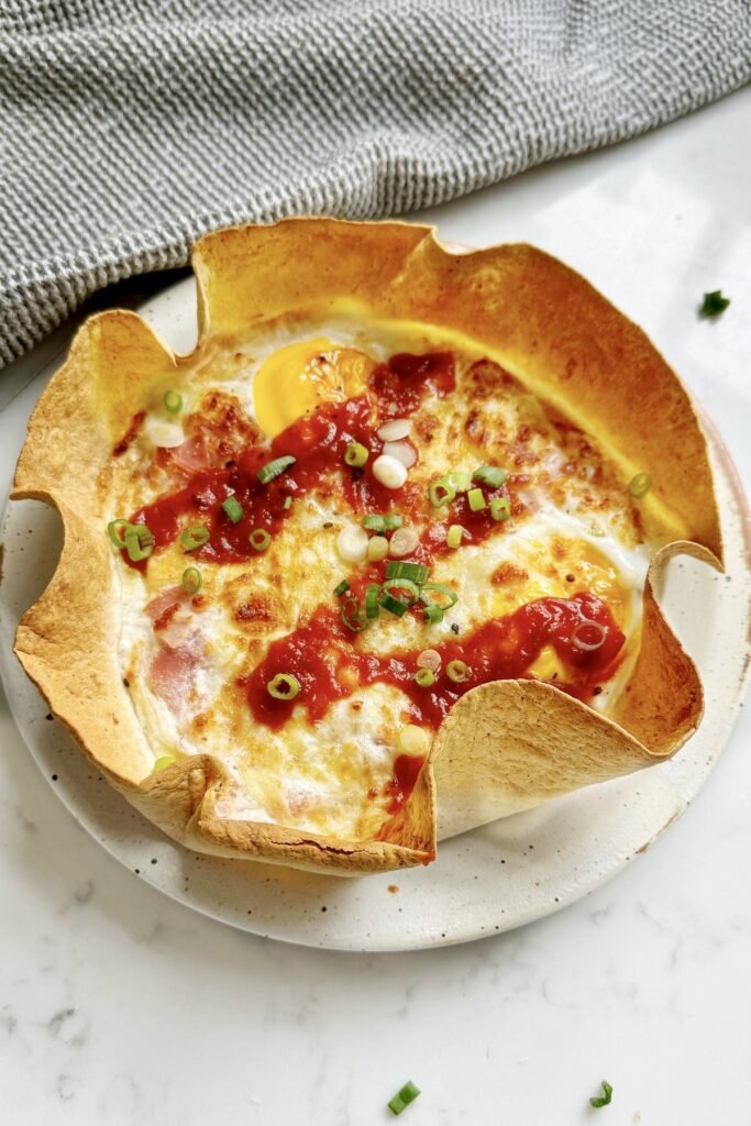 Ham and cheese tortilla quiche in a tortilla case on a speckled plate, topped with ketchup and spring onion