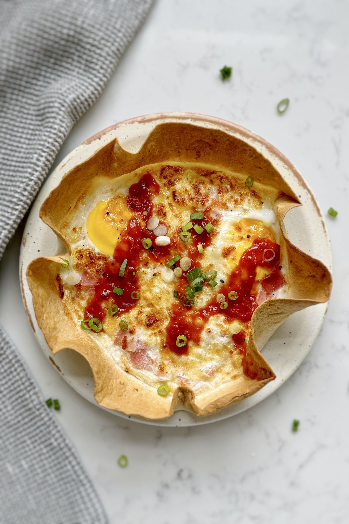 Ham and cheese tortilla quiche on a plate with a crisp ruffled tortilla edge and set egg centre