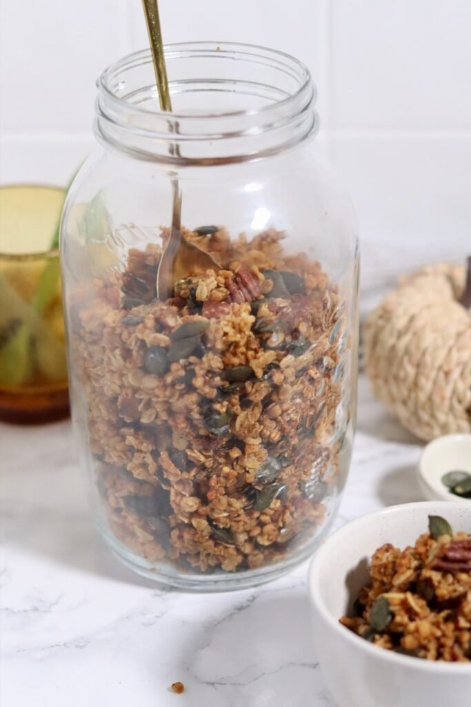 Homemade pumpkin granola being spooned into a glass storage jar