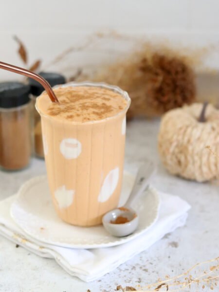 A tall glass of protein pumpkin smoothie with a copper straw and a spoon of cinnamon