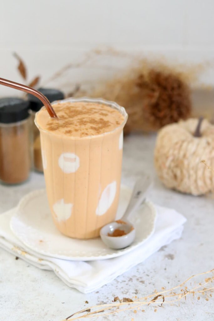 A tall glass of protein pumpkin smoothie with a copper straw and a spoon of cinnamon