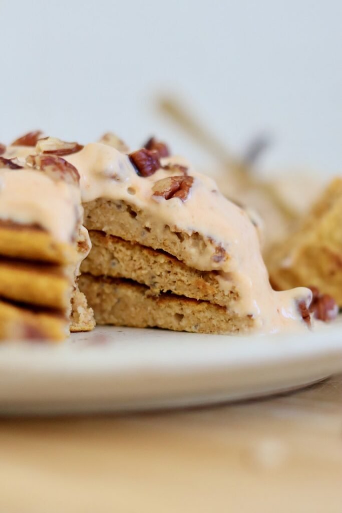 Stack of pumpkin protein pancakes cut open to show the fluffy layers, topped with pumpkin yoghurt and pecans