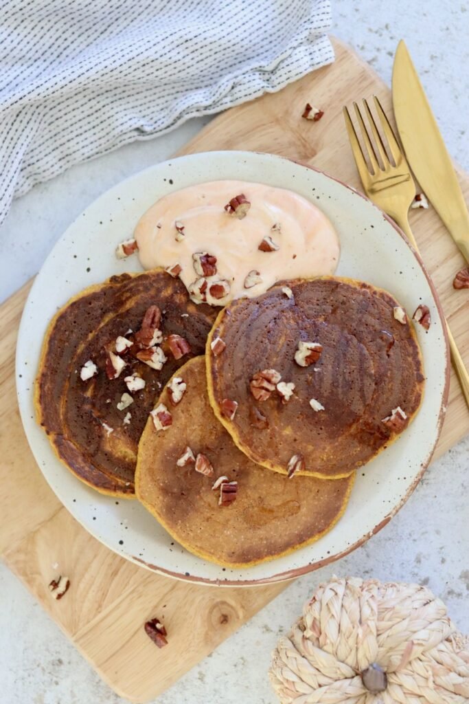 Three pumpkin protein pancakes fanned out on a speckled plate with gold cutlery
